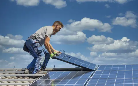Instalator montuje panele fotowoltaiczne na dachu. Optymalne ustawienie paneli wschód-zachód zapewnia maksymalne wykorzystanie energii słonecznej.