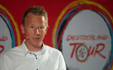 Fabian Wegmann spricht vor dem Logo der Deutschland Tour. Seine Vergangenheit mit Doping-Vorwürfen wirft einen Schatten auf seine Karriere.