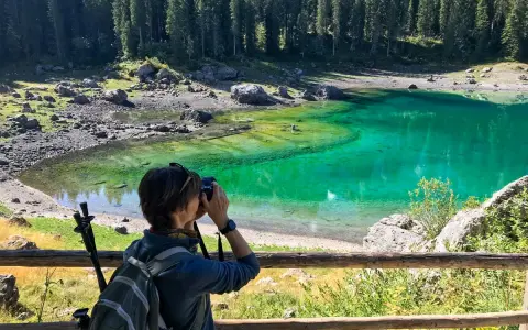 Donna con zaino e macchina fotografica cattura la bellezza del lago di Carezza, in Trentino Alto Adige.