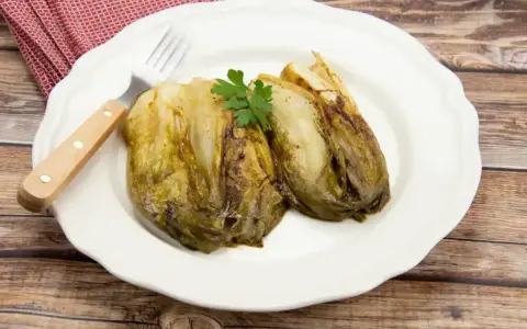 Deux endives caramélisées à la poêle, garnies de persil, sur une assiette blanche avec une serviette à carreaux rouges et une fourchette.