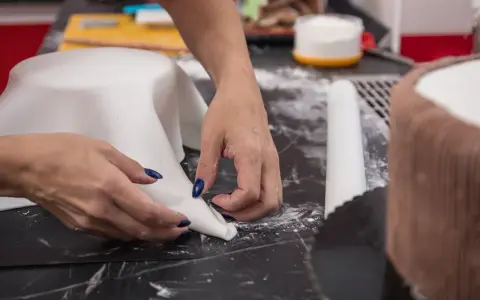 Hände formen weißen Fondant für eine Torte. Hier sind Tipps zum Fondant ausrollen für perfekte Ergebnisse.