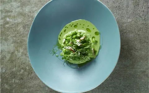 Délicieuse cuisson petit pois frais, servis dans une assiette bleue avec une émulsion verte et des éclats d'amandes.