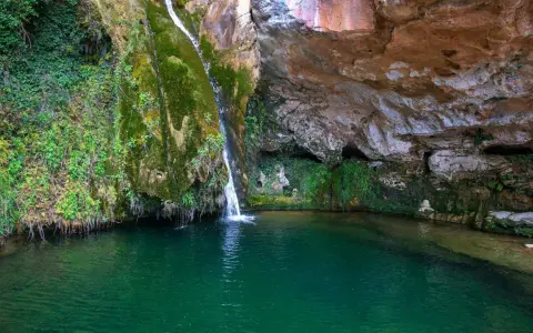 La cascada del río Carbo cae en una poza de agua verde esmeralda, rodeada de rocas cubiertas de musgo y vegetación exuberante.