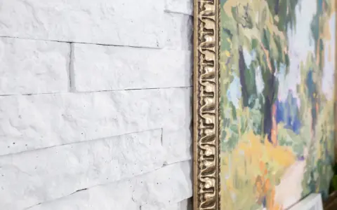 Un mur en pierre peint en blanc sert de toile de fond à un tableau aux couleurs vives, encadré d'or.