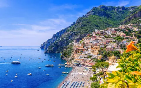 Färgstarka hus klättrar uppför bergssluttningen vid en livlig strand. Perfekt för din resa till Italien tips!