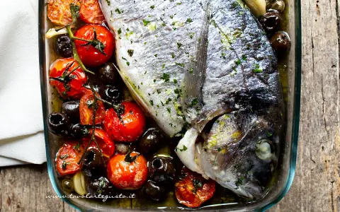 Filetti di orata al forno con pomodorini, olive nere e aglio, un piatto saporito e profumato.