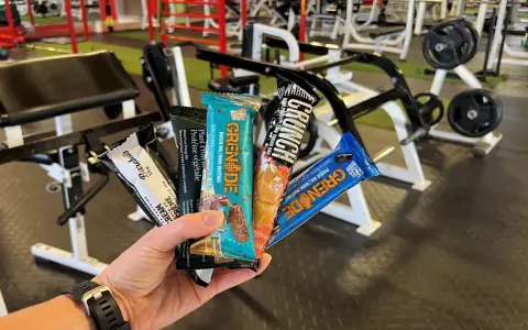 Une main tient plusieurs barres protéinées, parfaites comme collation avant ou après le sport, dans une salle de sport.