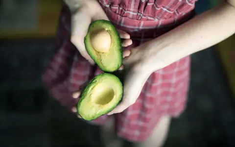 Hände halten eine aufgeschnittene Avocado, bereit für eine pflegende Avocado-Maske für die Haare.