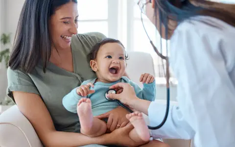 Glad mamma ser sitt barn få ett års vaccin. Läkaren lyssnar på barnets hjärta med stetoskop.