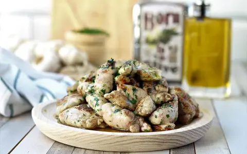 Deliciosas mollejas de cordero salteadas con perejil fresco, servidas en un plato de madera. Al fondo, aceite de oliva y ajos.