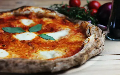 En perfekt pizza på grillen, med smält mozzarella och färsk basilika. Tomater och vitlök i bakgrunden.