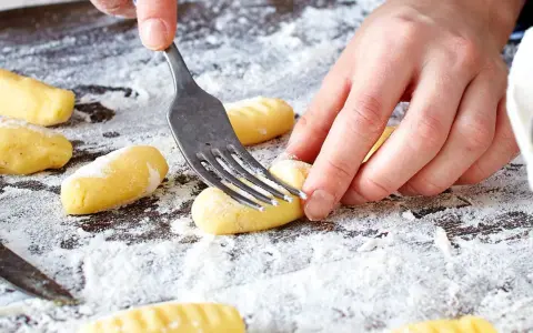 Hände formen mit einer Gabel die Rillen für original Gnocchi auf einer bemehlten Arbeitsfläche.