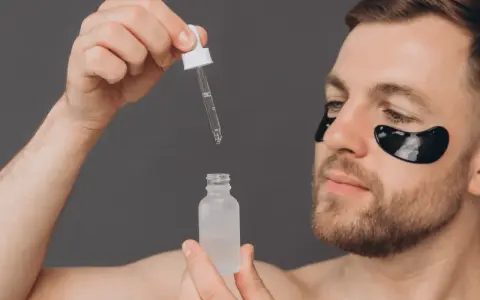 Homme appliquant un sérum, se demandant acide glycolique combien de fois par semaine. Patchs noirs sous les yeux pour un soin ciblé.