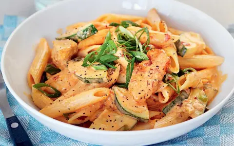 En skål med krämig penne med kyckling och zucchini, toppad med salladslök. En riktigt god pasta!