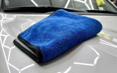 En blå torkhandduk ligger på en skinande vit bilhuv. Perfekt för att torka av bilen efter tvätt.
