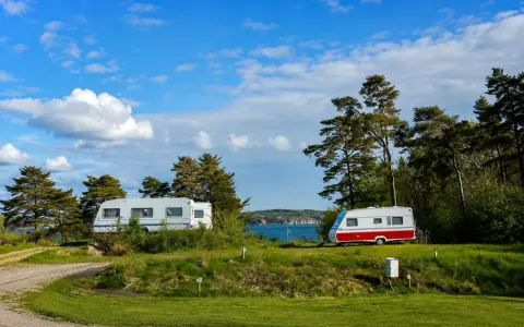 Två husvagnar på en grönskande campingplats vid havet i Lysekil. Blå himmel med vita moln.