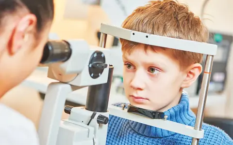 Chłopiec przechodzi komputerowe badanie wzroku u dzieci. Okulista bada jego oczy za pomocą specjalistycznego sprzętu.