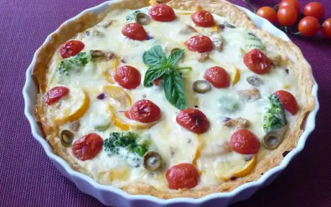 Pyszna tarta na słono z brokułami, pomidorkami koktajlowymi i oliwkami, udekorowana listkiem bazylii.