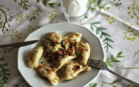 Pyszne pierogi ruskie z cebulką i boczkiem, gotowe do jedzenia. Obok widelec i nóż.