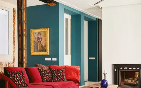 Sofá rojo vibrante con cojines estampados, pared azul petróleo y detalles rústicos. ¡Los mejores colores para pintar una casa!