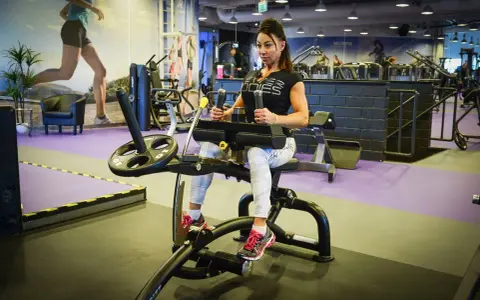 Kvinna tränar på gymmaskin. Hon har på sig träningskläder och fokuserar på sin träning. Hon verkar vara en seriös atlet som tar sin vad press på allvar.