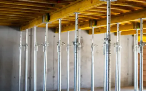 Metalowe podpory budowlane podtrzymują żółtą konstrukcję stropu. Wieniec budowlany w akcji.