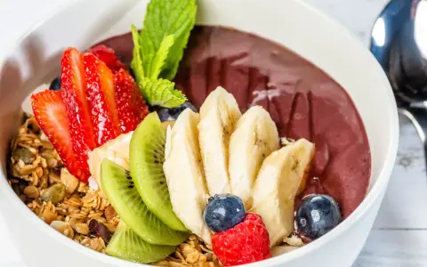 Acai-Schüssel mit Früchten, Granola und einem Hauch von Vitamin C. Erdbeeren, Bananen, Kiwi, Blaubeeren und Himbeeren machen diese Schüssel zu einem gesunden Genuss.