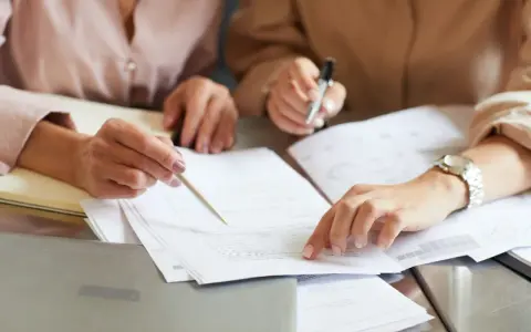 Dwie osoby analizują dokumenty, jedna wskazuje palcem na papier.