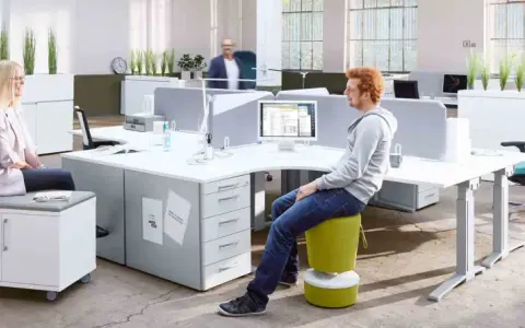 Un espace de travail open space moderne avec des bureaux modulables, des plantes vertes et des sièges colorés. Deux personnes discutent, une troisième travaille sur son ordinateur.