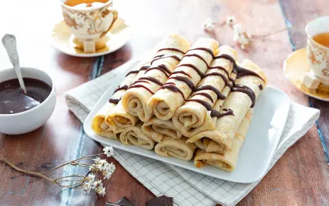 Crêpes roulées, nappées de chocolat, accompagnées d'une tasse de thé. Une recette crêpe raffinée pour un goûter gourmand.