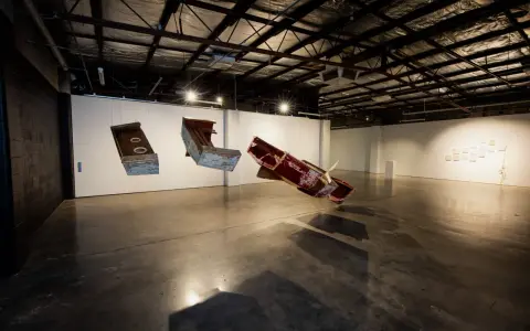 Suspended sculptures of weathered wood and metal hang in the spacious praxis gallery, casting long shadows on the concrete floor.