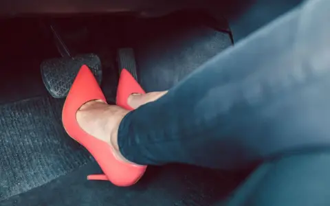 Piedi con tacchi rossi sui pedali dell'auto. Dimostra che si può guidare con i tacchi, con stile e sicurezza.