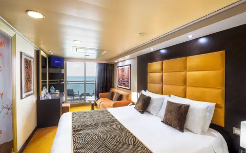 Interno di una cabina con balcone MSC Splendida: letto king-size, divano arancione, TV e vista mare.