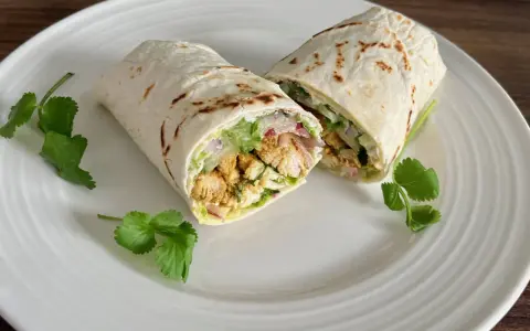 Kebab w tortilli z kurczakiem, warzywami i kolendrą na białym talerzu.
