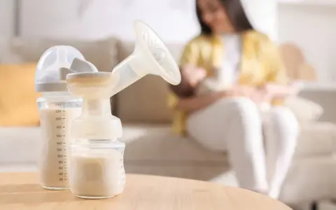 Biberon e tiralatte con latte materno, mentre una mamma allatta il suo bambino. Scopri come aumentare il latte materno in modo naturale.