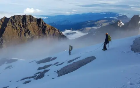 Dwóch alpinistów na ośnieżonym zboczu, w tle majestatyczne góry Ekwadoru, w tym najwyższy szczyt ekwadoru.