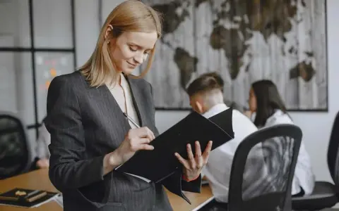 Kobieta w garniturze analizuje dokumenty, przygotowując się do ważnego spotkania. Jej zaangażowanie świadczy o profesjonalnym podejściu do stosunku pracy.