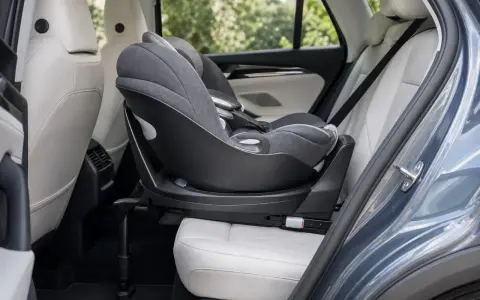 Silla de coche para bebé, instalada a favor de la marcha, con base giratoria y tapicería gris sobre asientos de cuero blanco en el interior de un vehículo.