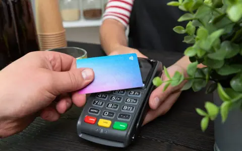 Pago sin contacto con una tarjeta prepago. Una mano acerca una tarjeta de colores a un terminal de pago.