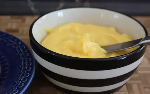 En skål med krämig, gul lemon curd, redo att bredas på en blå tallrik.