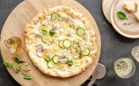 Pyszna pizza bianca z cukinią, cebulą i cytryną, podana na drewnianej desce.