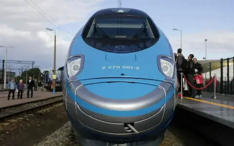 Pendolino Kraków Gdańsk cena: nowoczesny pociąg na torach, pasażerowie czekają na peronie.