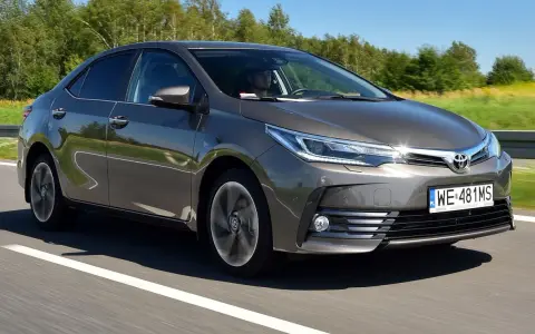 Szara Toyota Corolla E16 jedzie po drodze, za kierownicą siedzi mężczyzna.