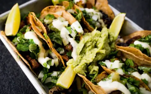 Saftige Tacos al Pastor mit Guacamole, Koriander und Limettenspalten.