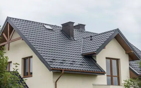 Nowoczesne opierzenie dachu z ciemnej blachodachówki, z dwoma kominami i okapem.