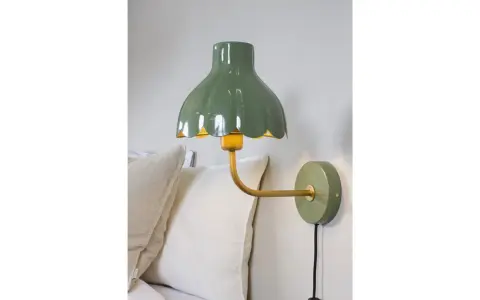 A green scalloped lampshade with a yellow interior, mounted on a gold arm attached to a green wall plate.