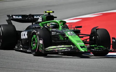 Ein grüner Formel 1 Bolide mit KICK-Sponsorenaufdruck rast auf der Rennstrecke. Die leistungsstarken Formel 1 Motoren lassen ihn über den Asphalt fliegen.