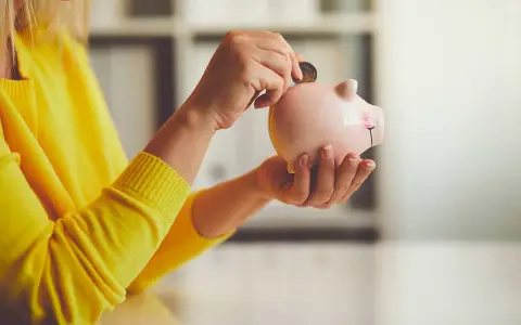 Persona con suéter amarillo deposita moneda en hucha. Un asesor fiscal te ayuda a ahorrar.