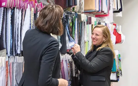 Deux femmes discutent devant un mur de tissus. L'une montre un échantillon de vêtement en fibre de bois à l'autre.
