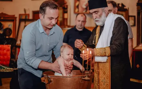 Chrzest dziecka w kościele. Ojciec trzyma niemowlę w miedzianej chrzcielnicy, a ksiądz polewa je wodą. To ważne chrzciny.